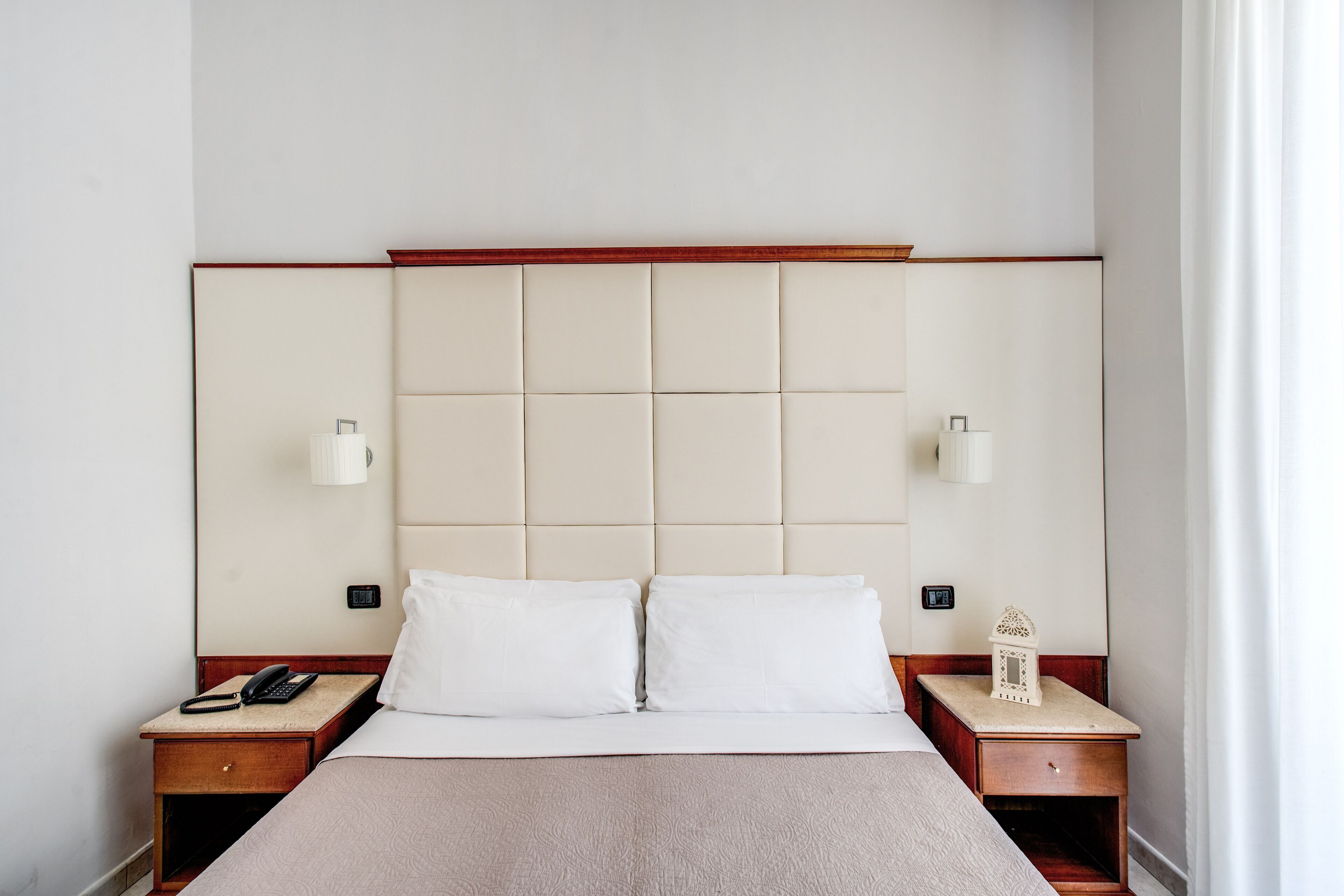 Habitación de hotel con una cama grande, dos mesitas de noche, un teléfono y una lámpara de pared.