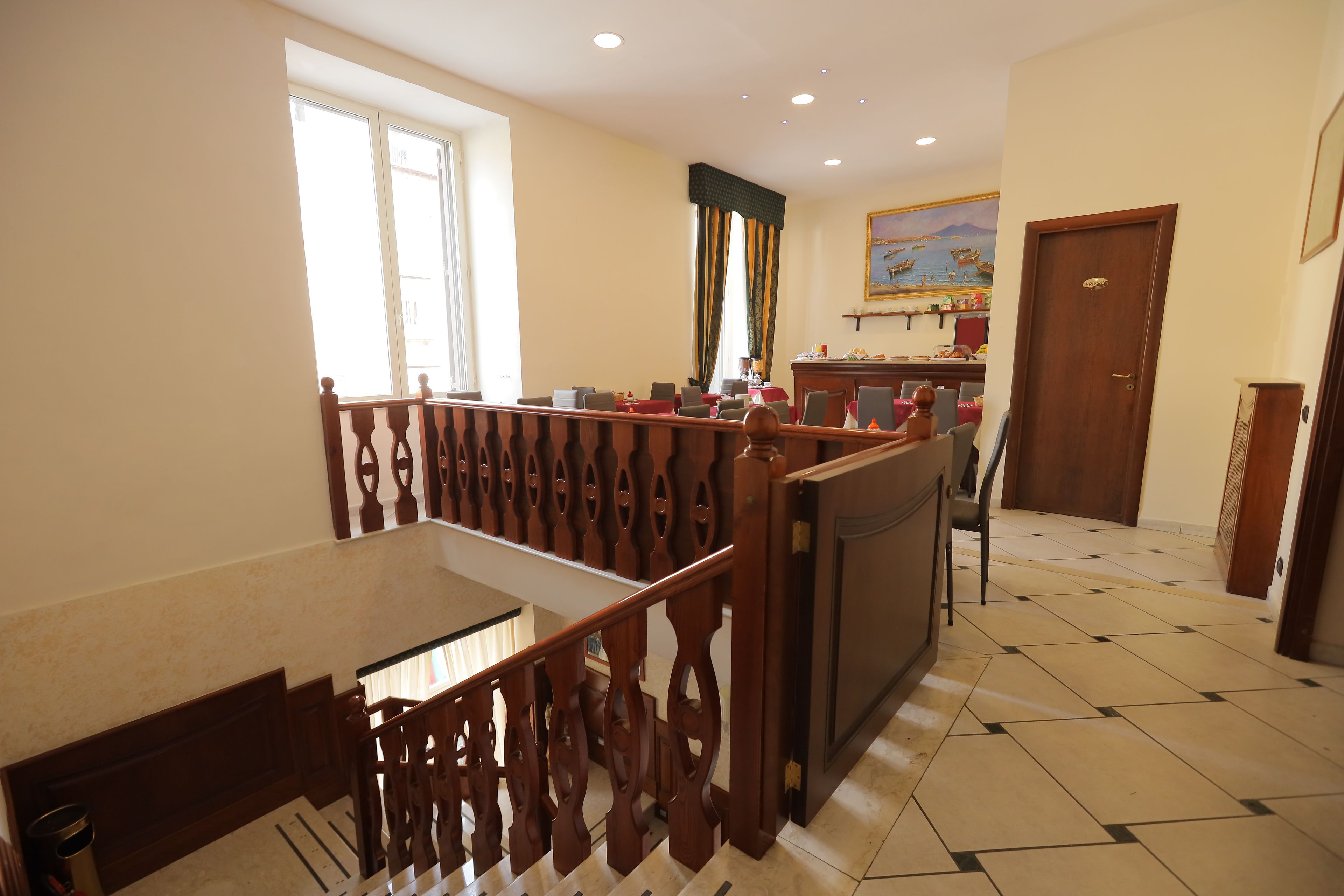 A hotel lobby with a staircase, a reception desk, and a dining area.