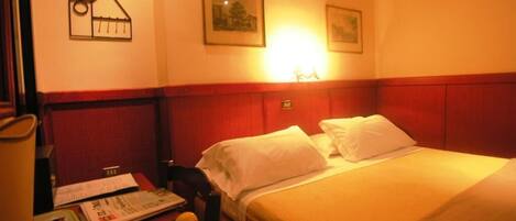 A hotel room with a bed, a nightstand with a lamp, a bowl of fruit, and a wall with a picture and a sign.