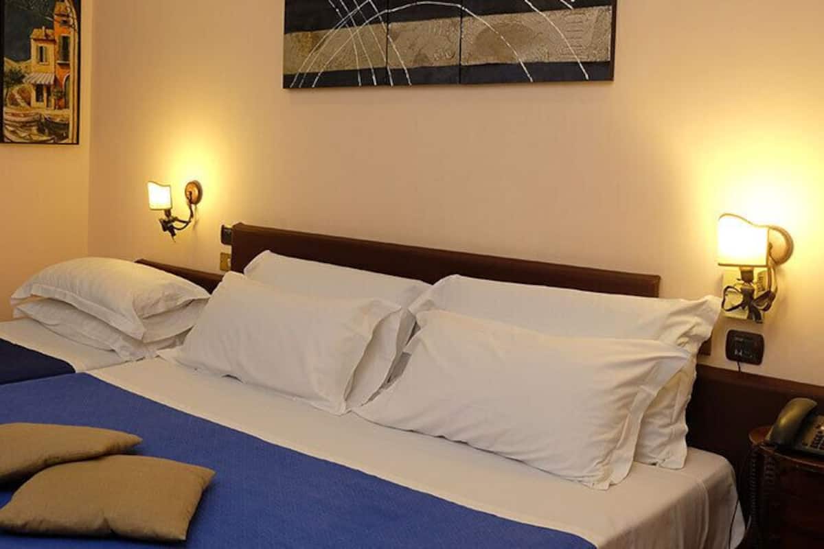A double bed with two pillows, a bedside table with a lamp, and a painting on the wall.