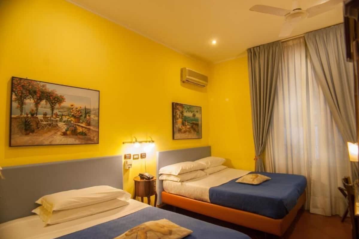 A hotel room with two beds, a ceiling fan, and two paintings on the walls.