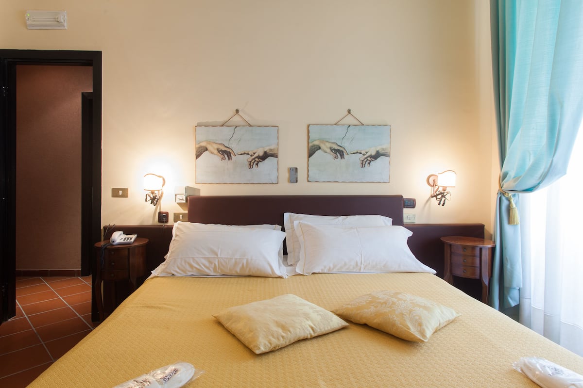 A hotel room with a large bed, two bedside tables, a nightstand, and two wall-mounted lamps.
