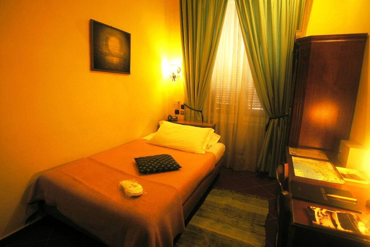 A hotel room with a bed, a desk with a lamp, a picture on the wall, and curtains.
