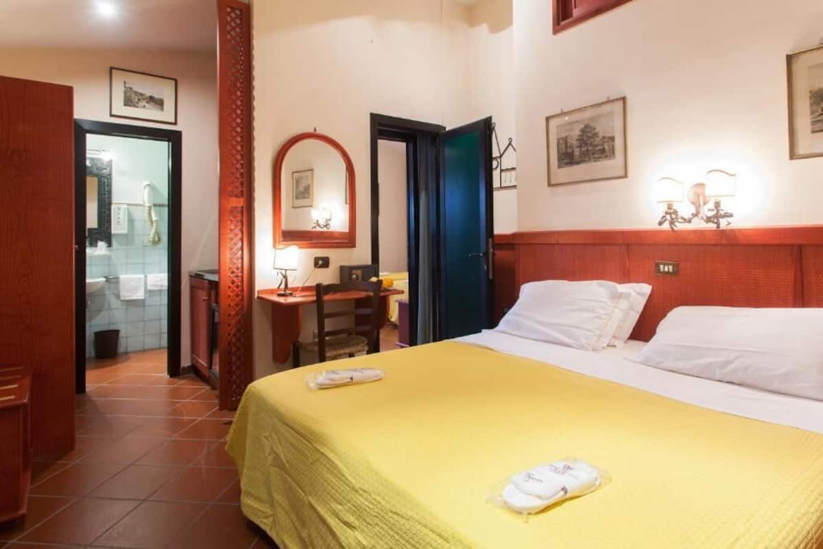 A hotel room with a bed, a desk, a chair, a mirror, and a bathroom visible through an open door.