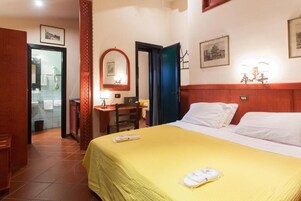 Una camera d'albergo con un letto, una scrivania, una sedia, uno specchio e un bagno visibile attraverso una porta aperta.