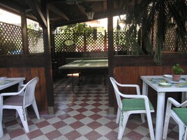 Un portico riparato con pavimento a scacchi, sedie di plastica bianca e un tavolo con una pianta in vaso.