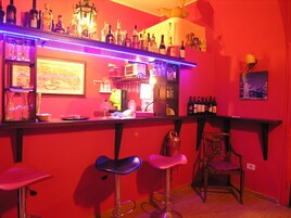 Angolo bar con una parete rossa, numerose bottiglie di liquori e sgabelli da bar.