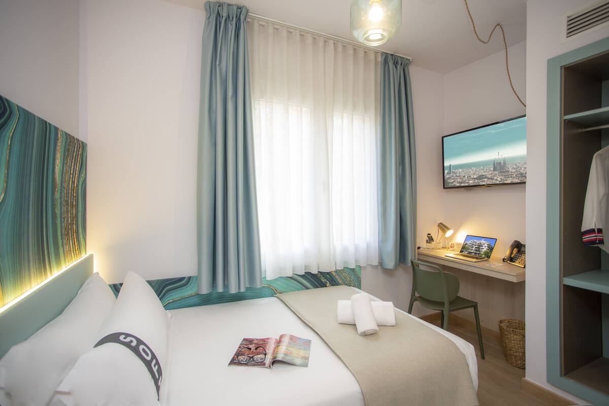 Habitación de hotel con cama, escritorio con computadora, silla y televisor en la pared.