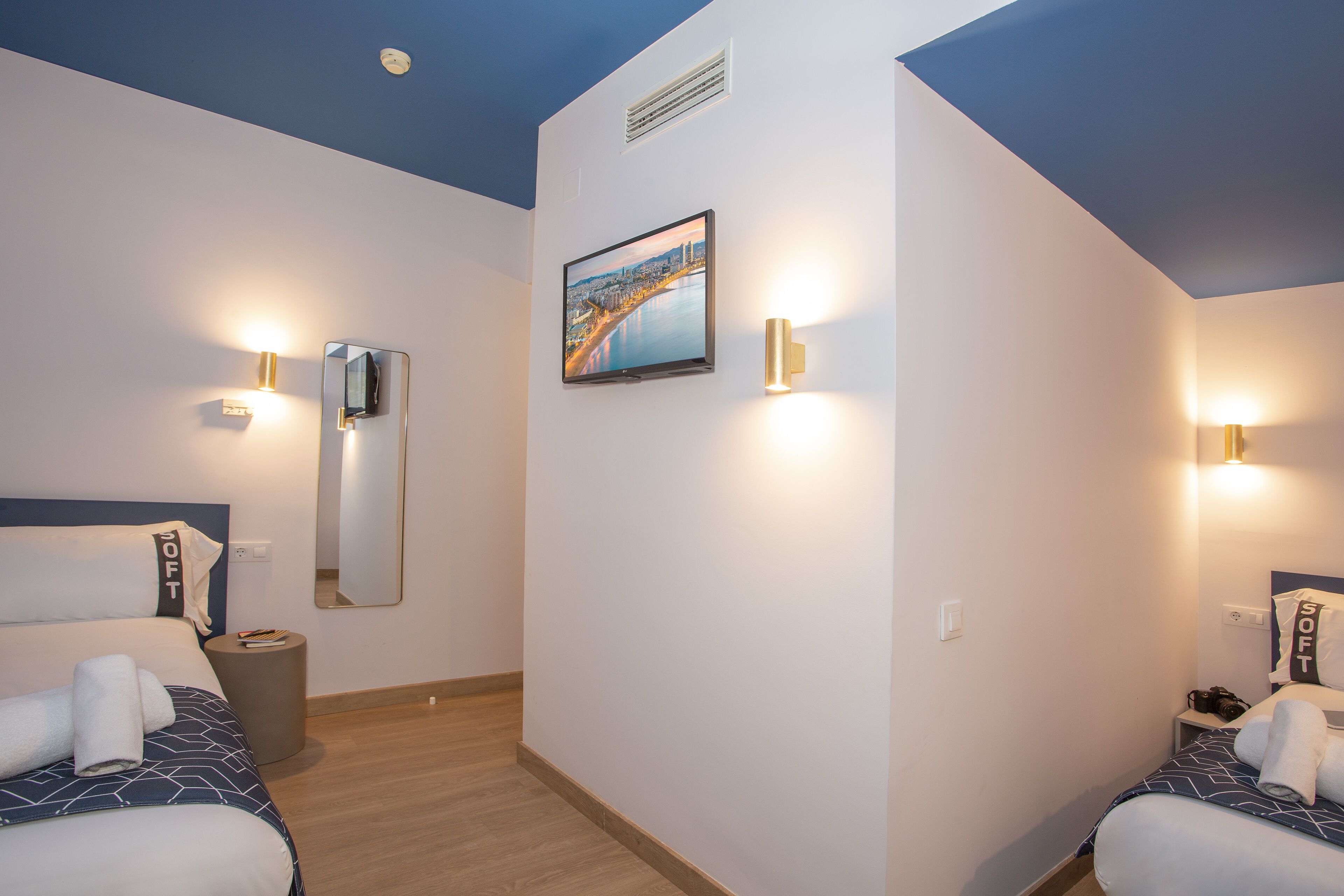 Habitación de hotel con dos camas, un espejo grande, un cuadro enmarcado y luces fijadas a la pared.