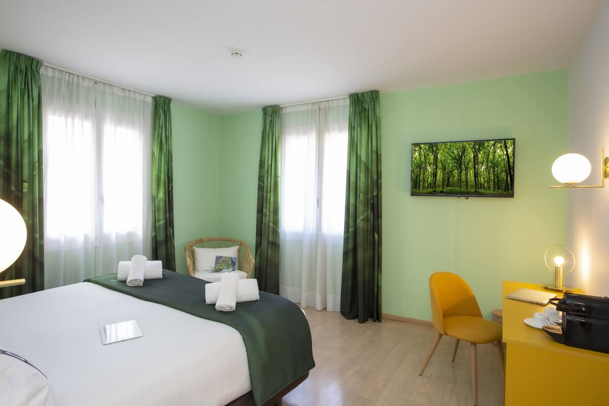 Habitación de hotel con cama, escritorio, silla, lámpara de escritorio y un cuadro en la pared.