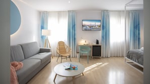 A modern hotel room with a grey sofa, a round coffee table, a wicker chair, a desk with a laptop, and a bed with a patterned duvet. - Casual Colours Barcelona Hotel by Casual Hoteles (Barcelona)