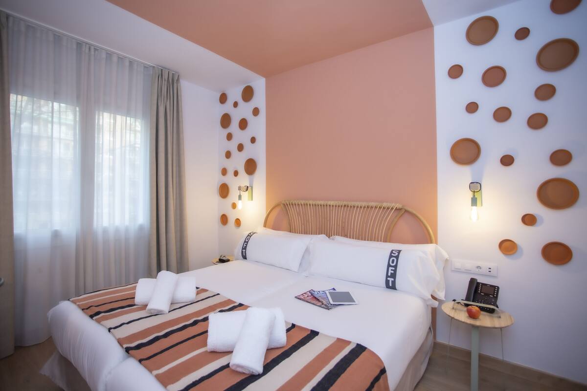 Habitación de hotel con una cama, una mesita de noche con un teléfono y fruta, y una pared decorada con adornos circulares.
