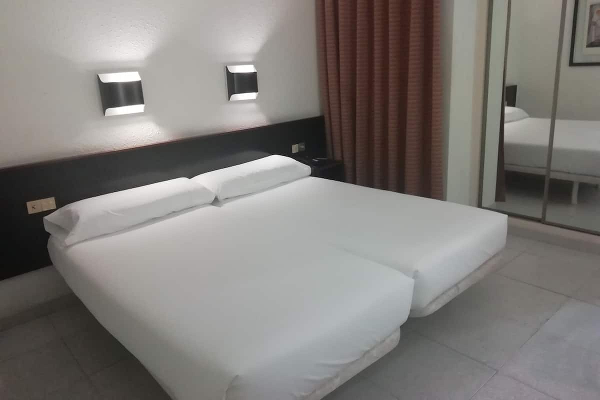 A neatly made bed with white linens, a dark headboard, and two wall-mounted lights.
