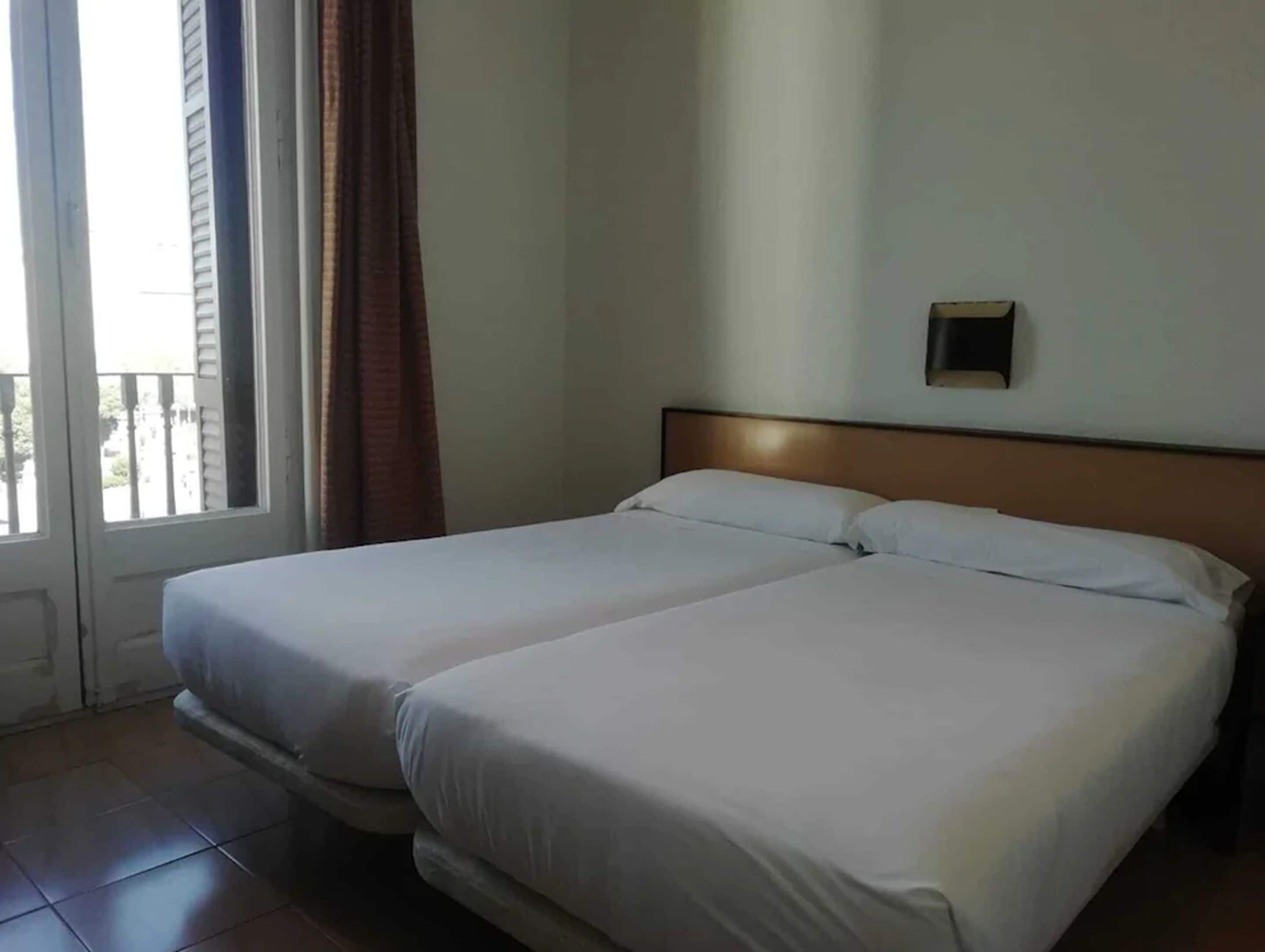 Une chambre d’hôtel avec deux lits, une fenêtre avec des rideaux et une vue sur l’extérieur.