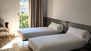 Een hotelkamer met twee bedden, een plafondventilator en uitzicht op een gebouw door een raam.