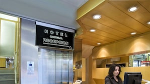 Een hotel receptie met een receptiebalie, een digitaal scherm en een lift.