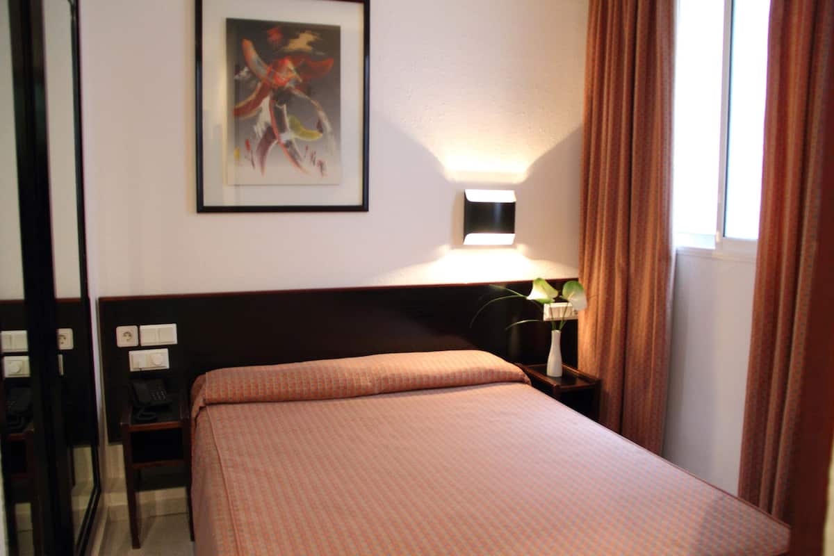 A hotel room with a bed, bedside table, lamp, and artwork on the wall.