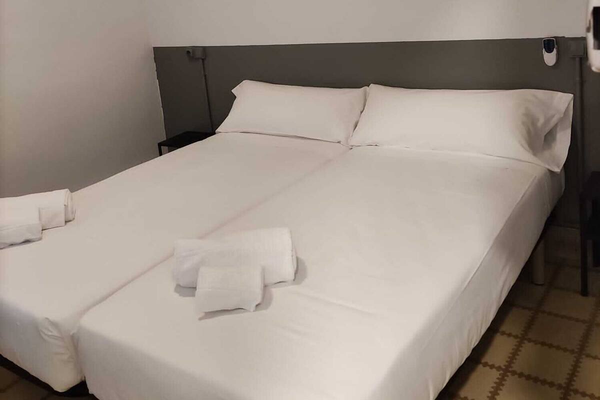 A double bed with white linens and towels, a headboard, and a tiled floor.