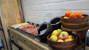 A buffet counter with various food items including meats, cheeses, fruits, and beverages.