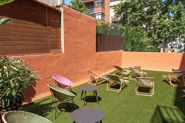 A rooftop terrace with artificial grass, several lounge chairs, and a small table.