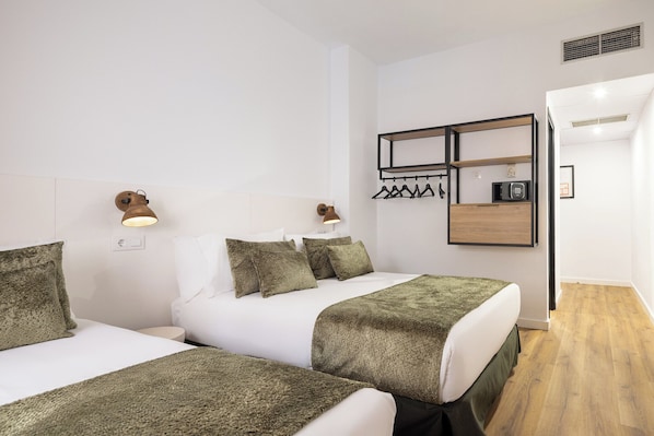 Habitación de hotel con dos camas, perchero, microondas y una mesita.