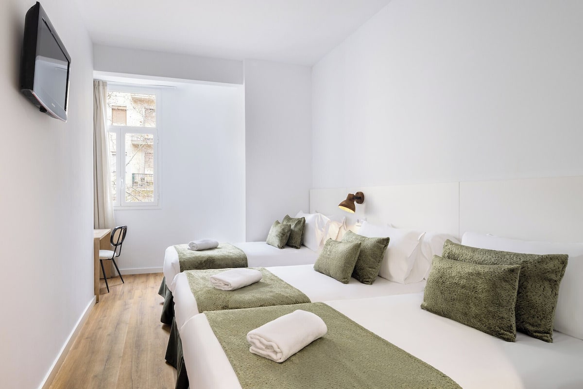 Een hotelkamer met twee bedden, een bureau, een stoel en een aan de muur bevestigde televisie.