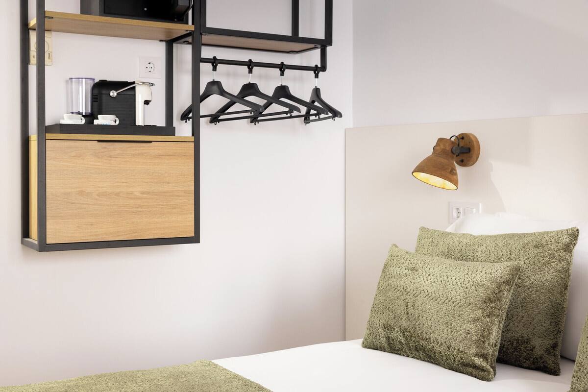 Een slaapkamer met een houten kast, een wandlamp en een bed met groene kussens.