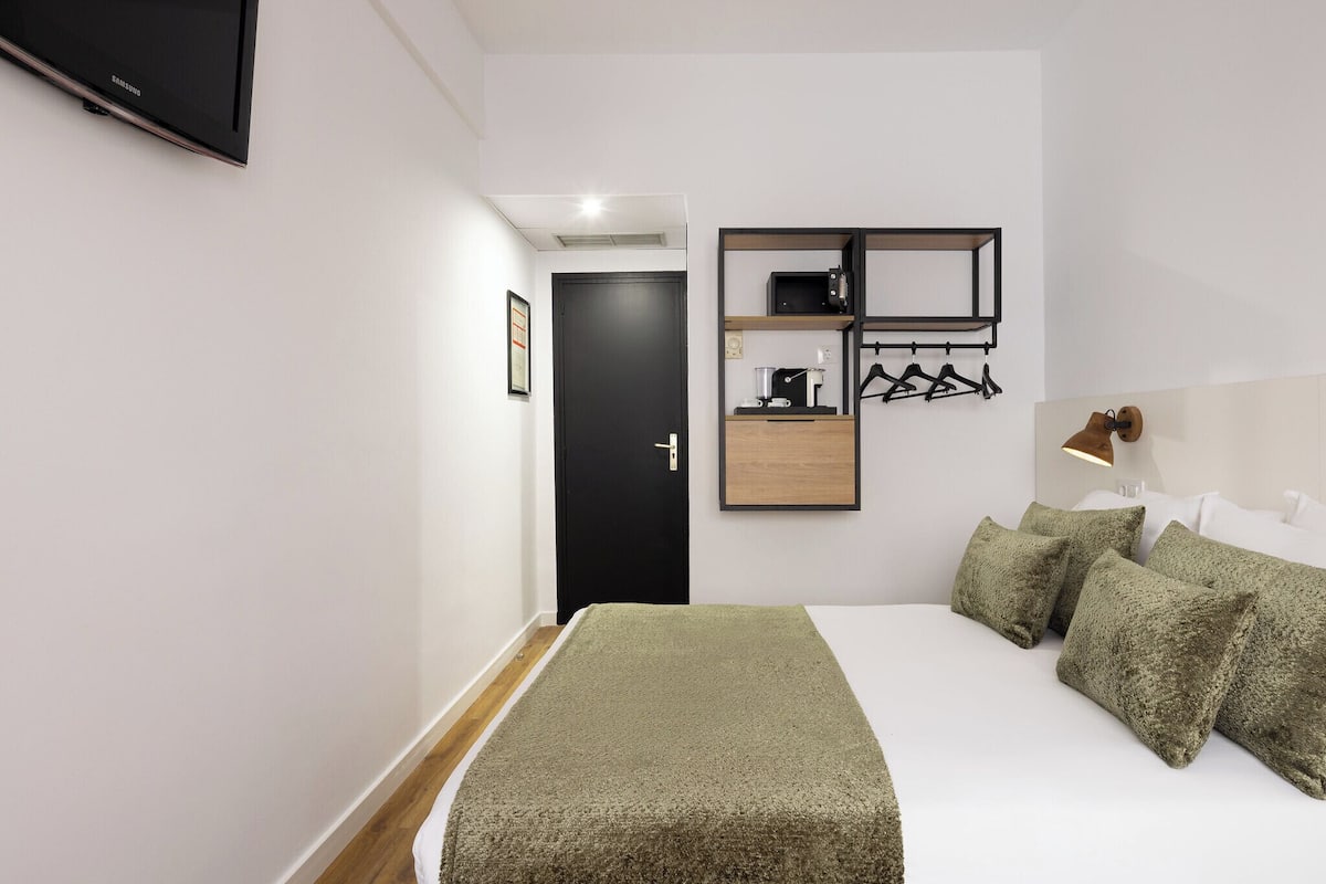 Een moderne hotelkamer met een bed, een flatscreen televisie, een koffiezetapparaat en een wandplank met een magnetron en kledinghangers.