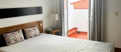 A hotel room with a large bed, a nightstand, a lamp, an air conditioning unit, and a framed picture on the wall.