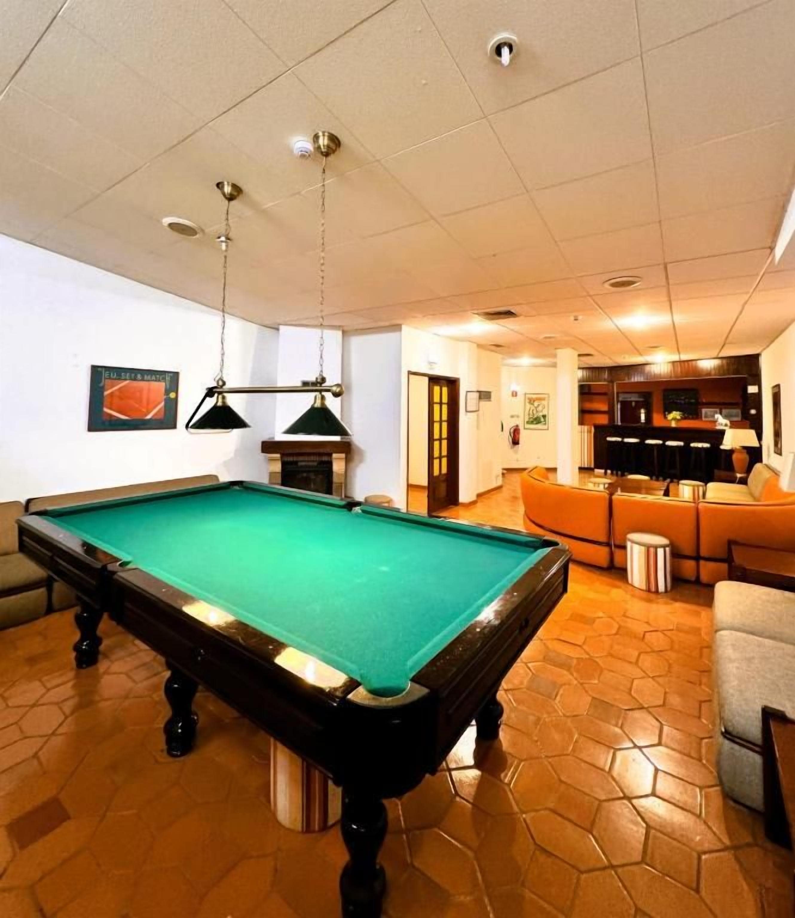 Een pooltafel in een ruimte met een betegelde vloer, een bank en een lamp.