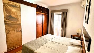A hotel room with a bed, a wooden wardrobe, a map on the wall, and a window with curtains.