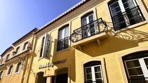A yellow building with a sign reading "Hotel Lygosmar." It features multiple windows, a balcony with ornate black railings, and a cobblestone street in front. - Lagosmar Hotel (Lagos)