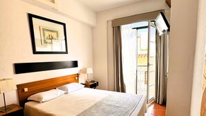 A hotel room with a large bed, a nightstand with a lamp, a framed picture on the wall, and a view of the outside through a window with curtains. - Lagosmar Hotel (Lagos)