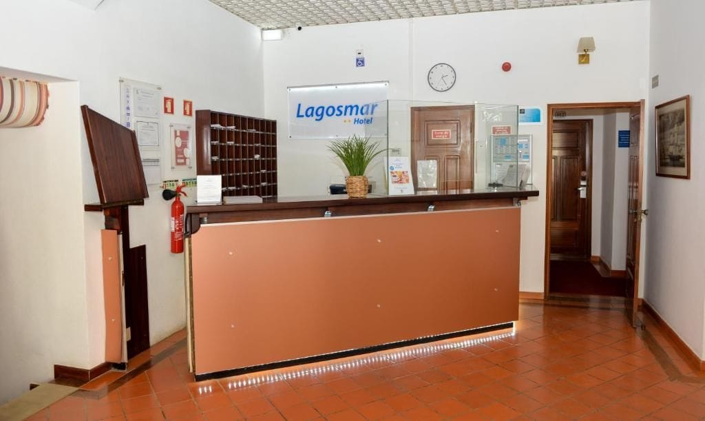 A hotel reception area with a reception desk, a clock, and a sign for 'Lagosmár Hotel'.