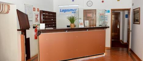 A hotel reception area with a reception desk, a clock, and a sign for 'Lagosmár Hotel'.