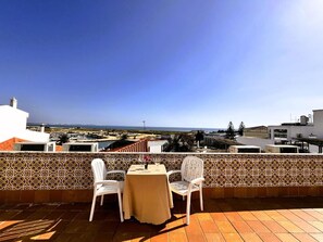 Una terraza con dos sillas blancas y una mesa, con vista a un paisaje costero.