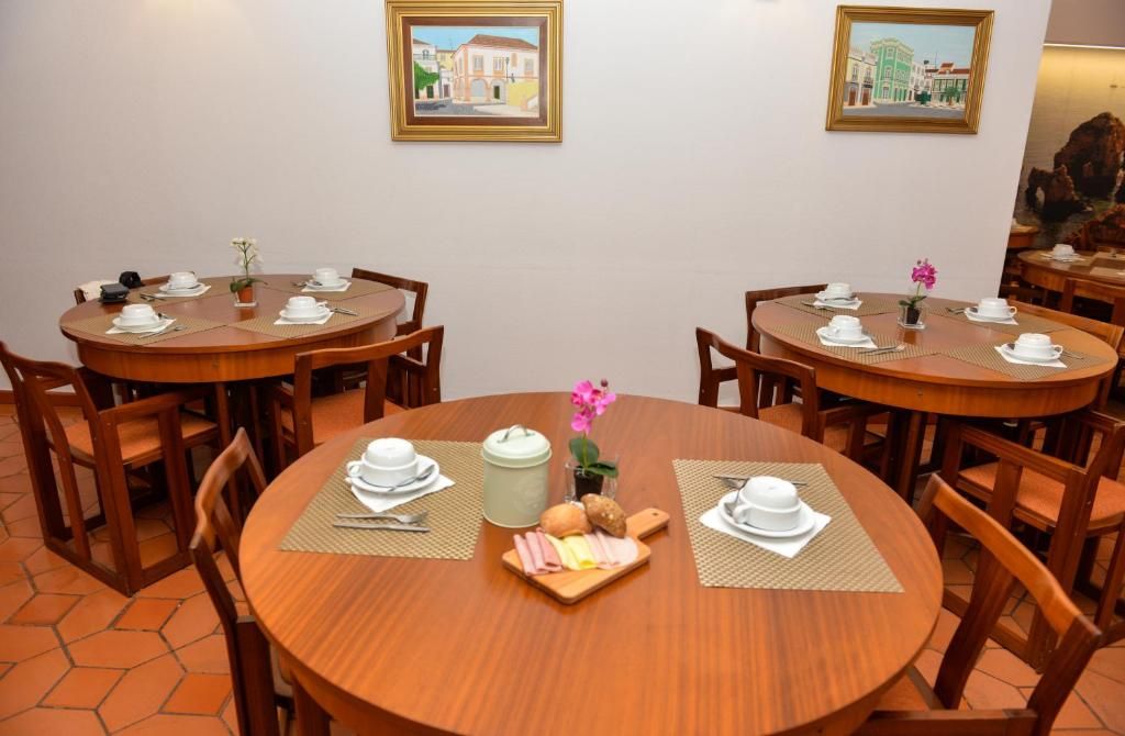 Un espace repas avec des tables rondes en bois, chacune agrémentée d’une nappe blanche, de couverts et d’un petit arrangement floral.