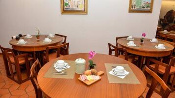 A dining area with round wooden tables, each set with white plates, cutlery, and a small centerpiece.