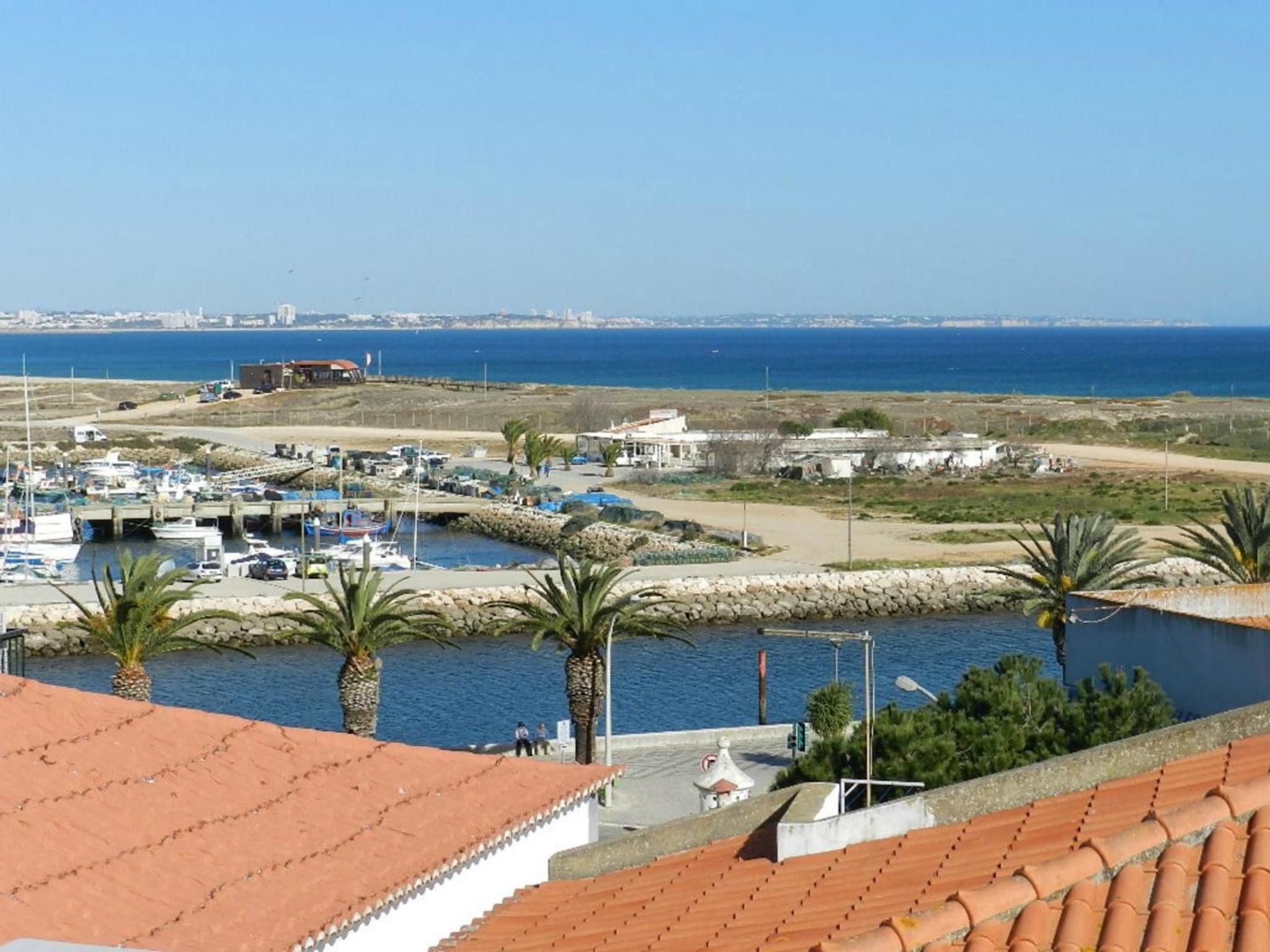 Un puerto costero con barcos, vista despejada del mar y un horizonte urbano lejano.