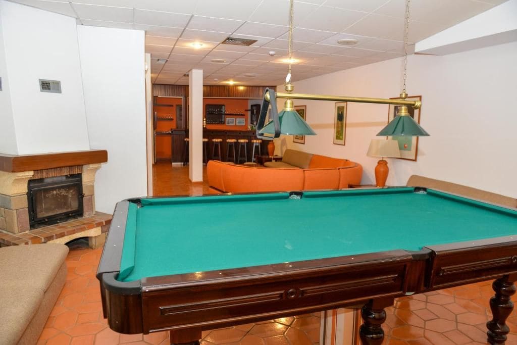A pool table with a green felt surface, a fireplace, and a bar area in the background.