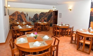 A dining area with multiple round tables, each set with white tableware and a vase of flowers. - Lagosmar Hotel (Lagos)