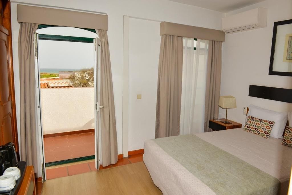 Habitación de hotel con una cama, una mesita de noche, una lámpara y vistas al exterior.