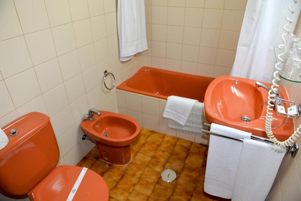 A bathroom with a toilet, bidet, bathtub, and sink, all in a matching orange color.