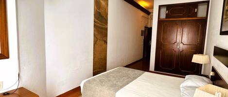 A hotel room with a bed, a TV mounted on the wall, a wooden desk, and a wardrobe.