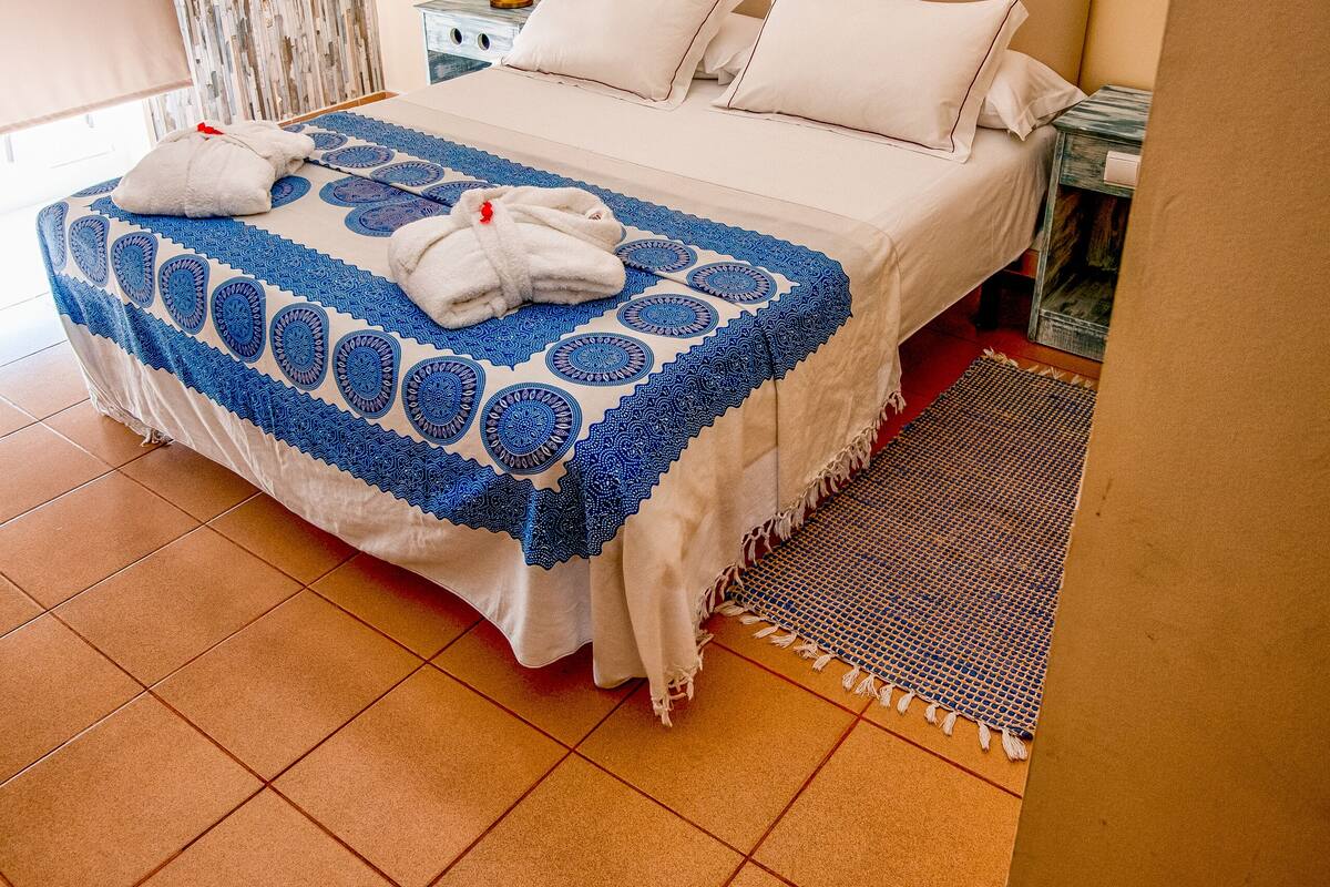 A neatly made bed with a blue and white patterned bedspread, a bedside table with a lamp, and a mirror on the wall.