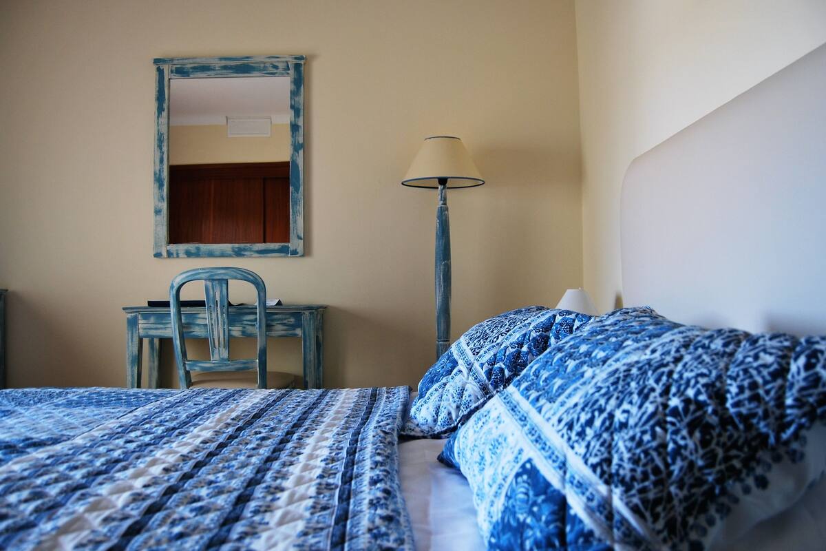 A bedroom with a bed, a desk, a chair, a lamp, and a mirror.