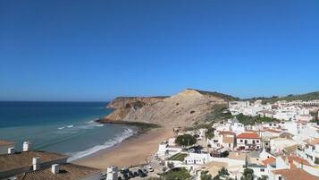 A coastal town with white buildings, a beach, and a prominent hill.