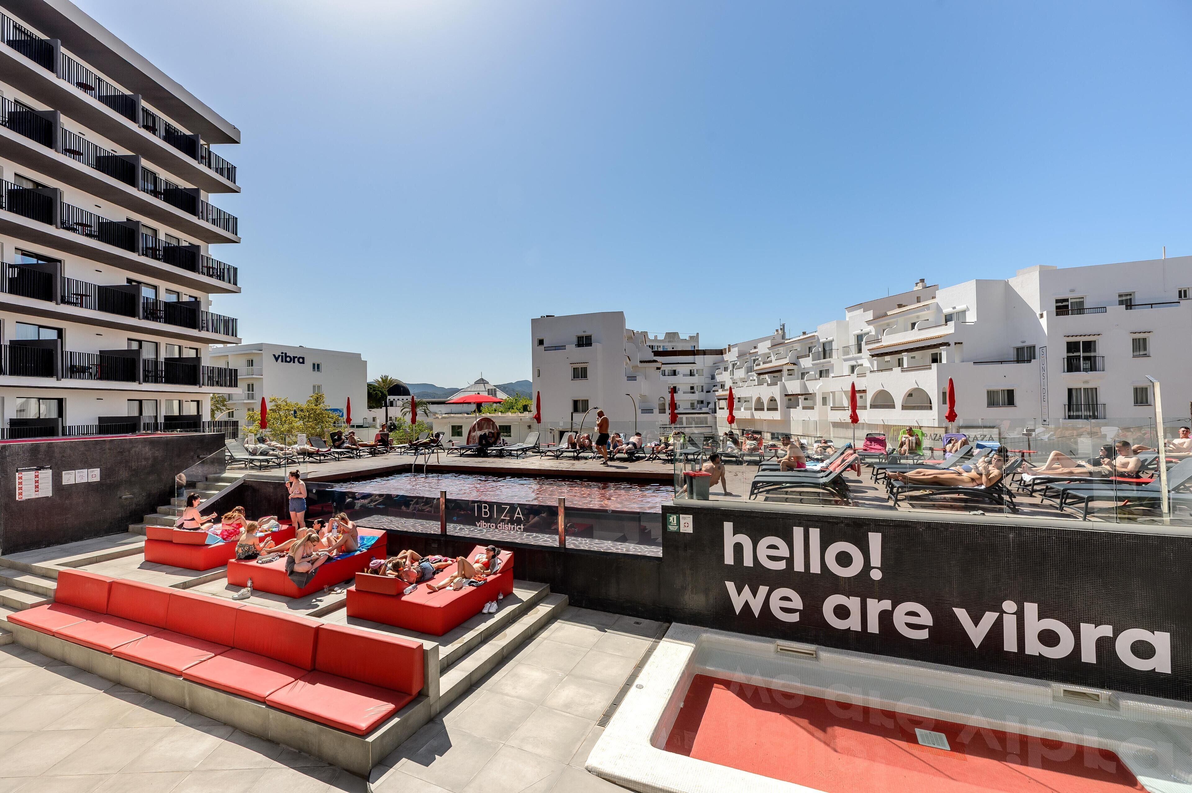 A rooftop pool area with red seating and a large digital screen displaying "hello! we are vibra".