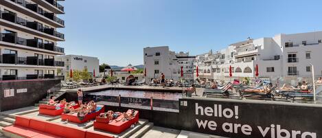 A rooftop pool area with red seating and a large digital screen displaying "hello! we are vibra".