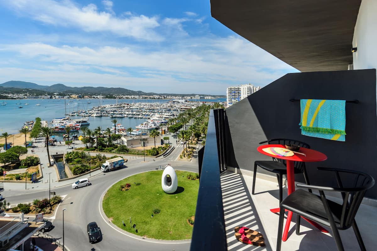A balcony with a view of a marina, a roundabout, and a building with a blue and yellow towel hanging.